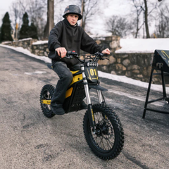 Young rider seated on a Classic yellow Heybike Villain on a paved road.