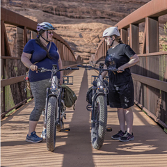 Two cyclists standing with Heybike Alpha electric bikes on a wooden bridge.