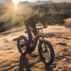 Rider using the Heybike Hero electric bike on a rocky desert trail at sunset.