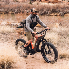 Rider using an orange Heybike Hero electric bike across dry terrain.