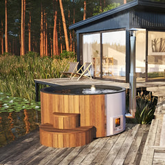 Wooden hot tub on a wooden deck by a modern house with a forest view.