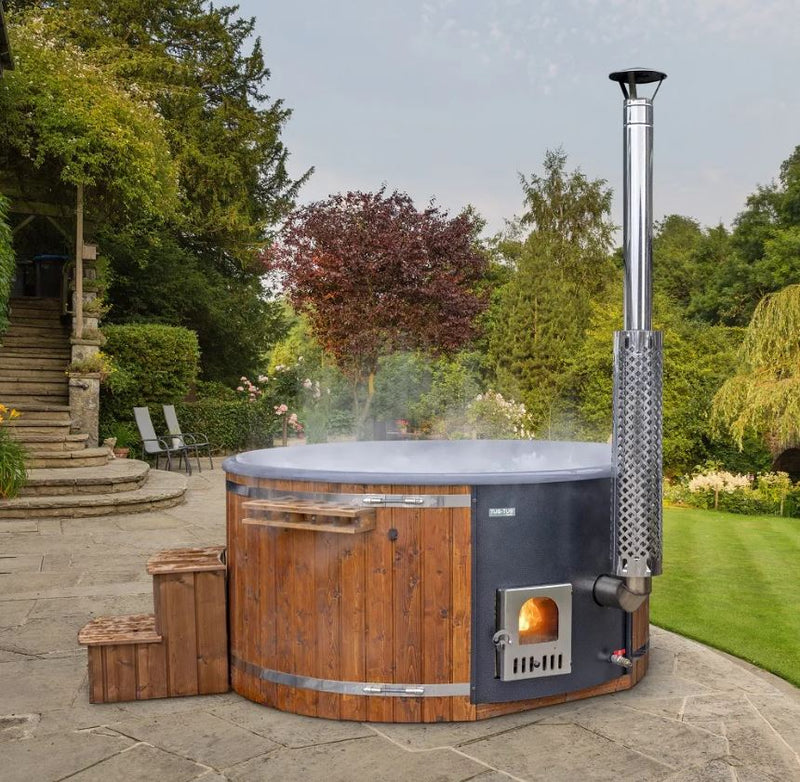 Wood-fired hot tub in a garden setting with trees and a stone pathway.